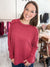 A woman smiling while wearing a ribbed long-sleeve top in a dusty rose pink color, standing inside what appears to be a boutique or clothing store.