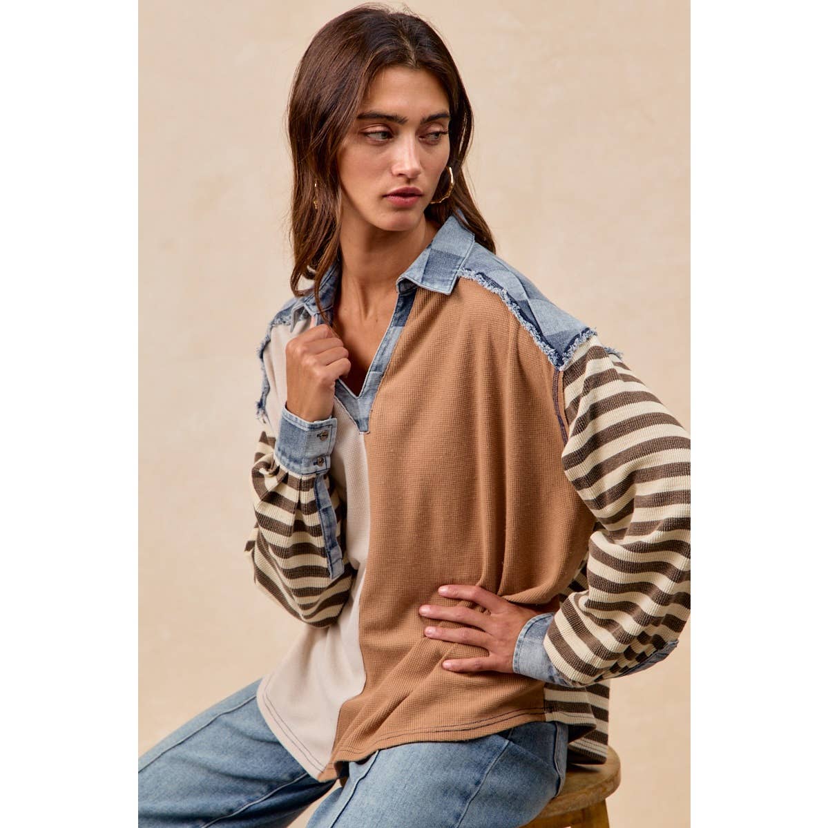Woman wearing a layered outfit with a brown shirt, striped sleeves, and denim accents on a beige background