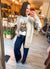 A woman takes a mirror selfie in a boutique, wearing a light beige knit cardigan over a white graphic t-shirt and dark blue wide-leg jeans.
