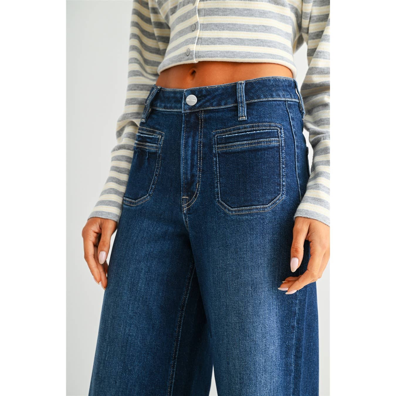 A person wearing dark blue high-waisted wide-leg jeans with a gray and white striped long-sleeve crop top, shown from the chest down against a light gray background.