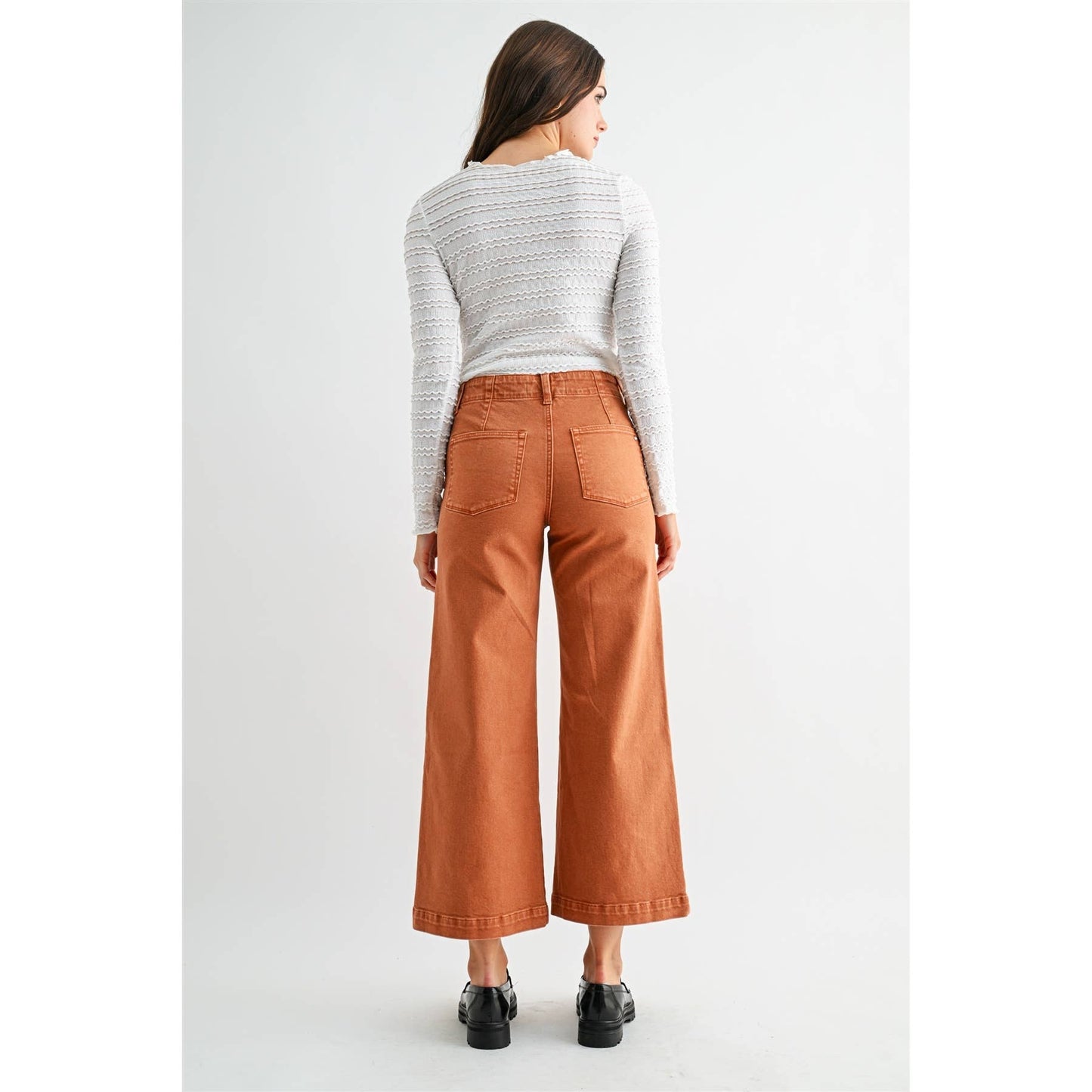 Woman wearing brown wide-leg pants and a light gray sweater on a white background