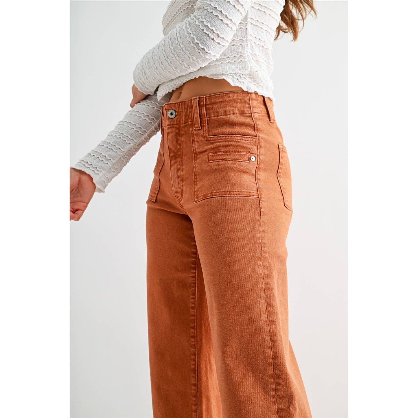 Person wearing orange pants and a white sweater on a plain background