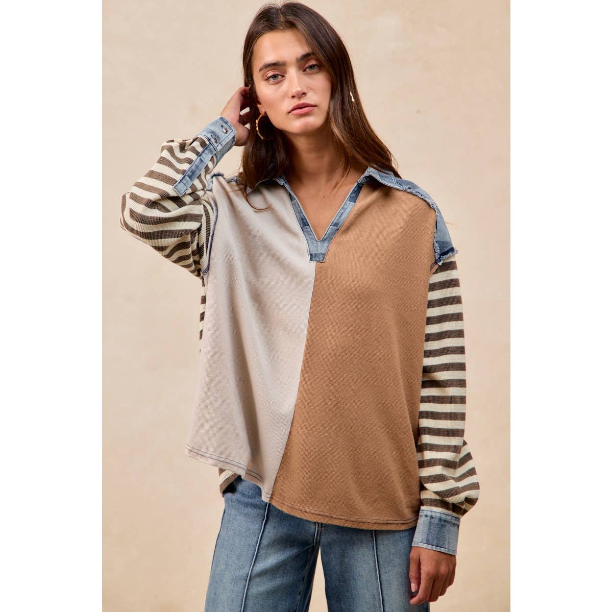 Woman wearing a long-sleeve shirt with color-blocked design and striped sleeves against a beige background