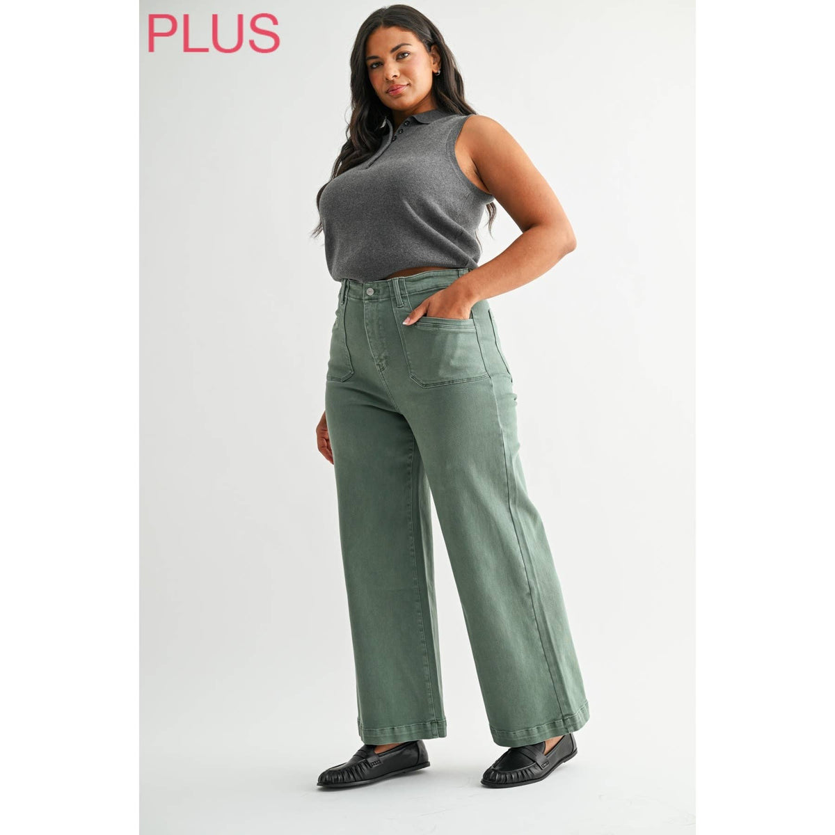 Woman wearing green wide-leg jeans and a gray top on a white background