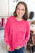 A woman smiling while wearing a bright pink mineral-wash long-sleeve sweatshirt with a chest pocket, paired with blue jeans in a boutique setting.