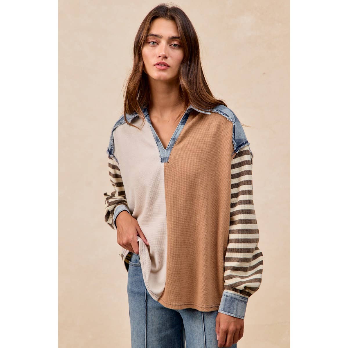 Woman wearing a color-blocked long-sleeve shirt with denim accents on a beige background